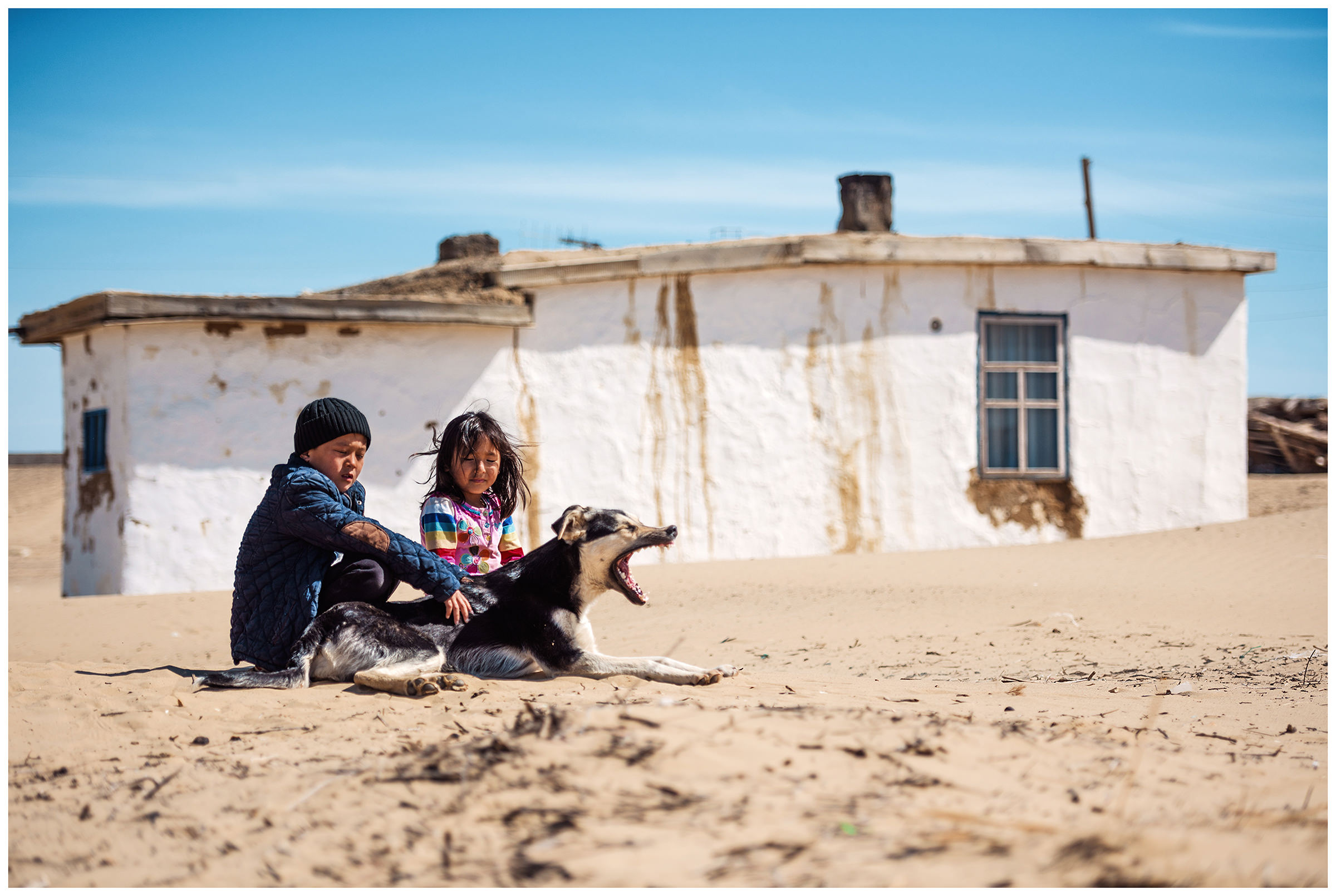A boy and a girl sit with a dog in front of a house in the fishing village Akespe