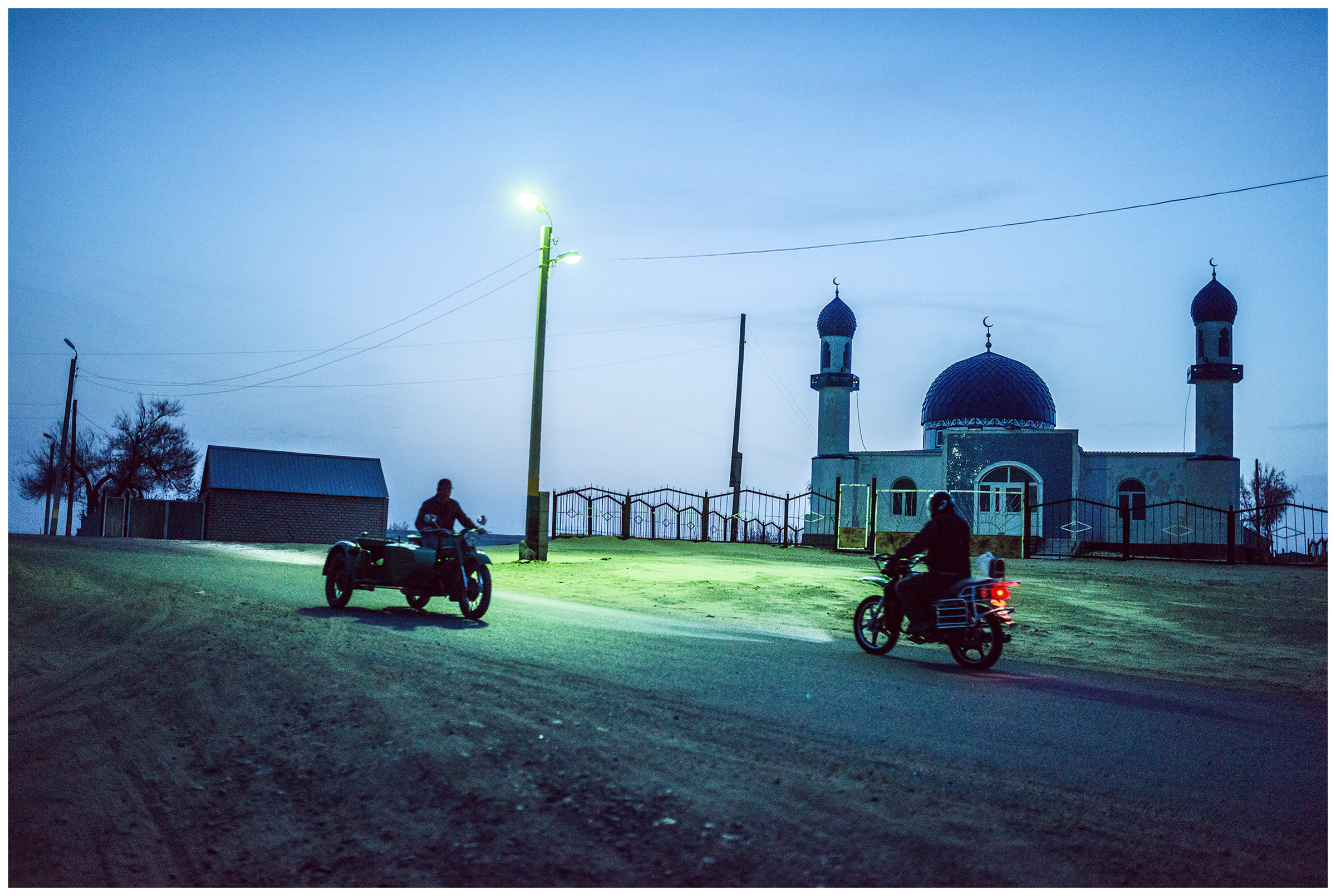Two motorbikes ride in front of a mosque late in the evening in the fishing village Bogen