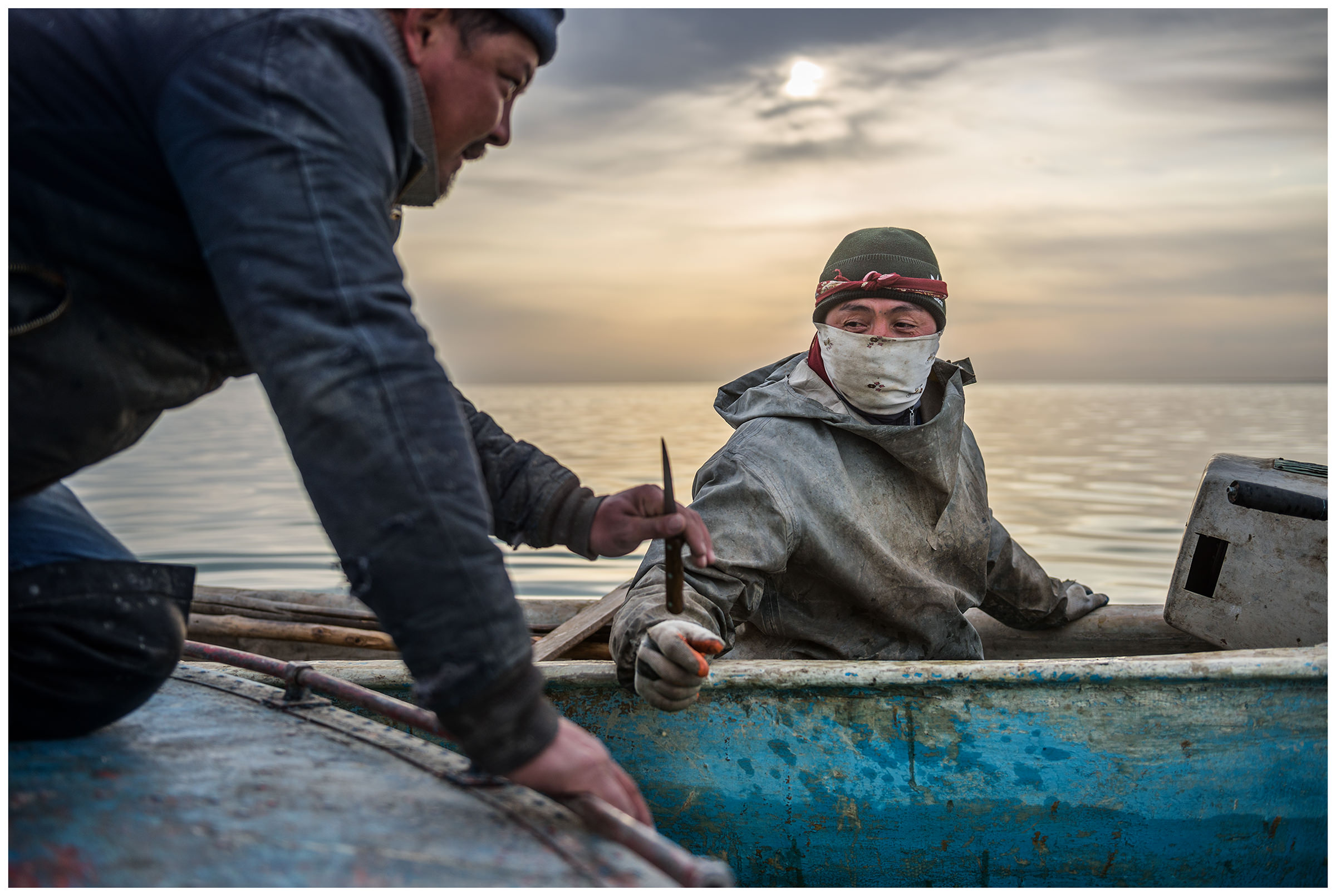 A fisherman hands over a knife to another fisherman