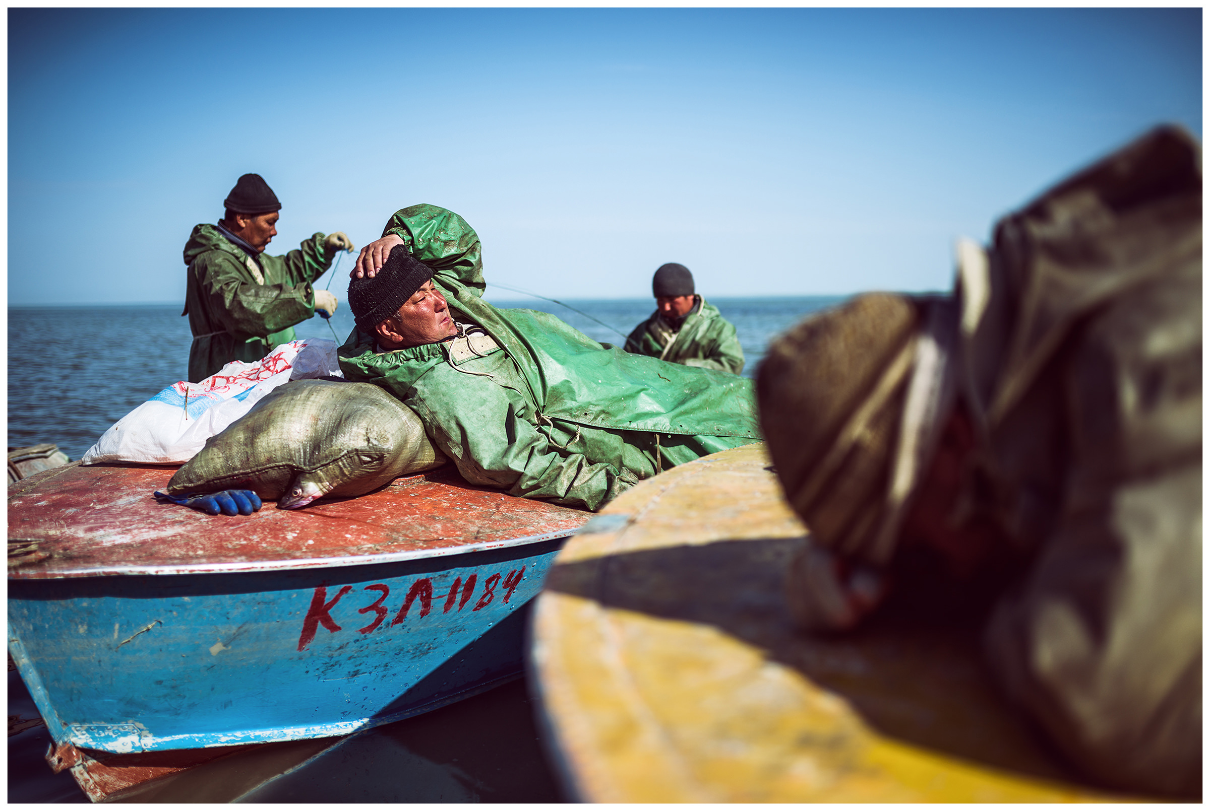 A fisherman lies on a sack of fish in his boat