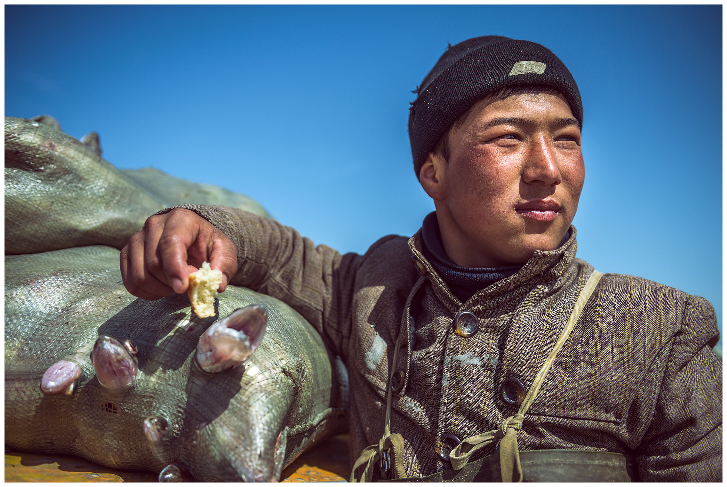 A young fisherman takes a break in front of a boat with a bag of fish on it