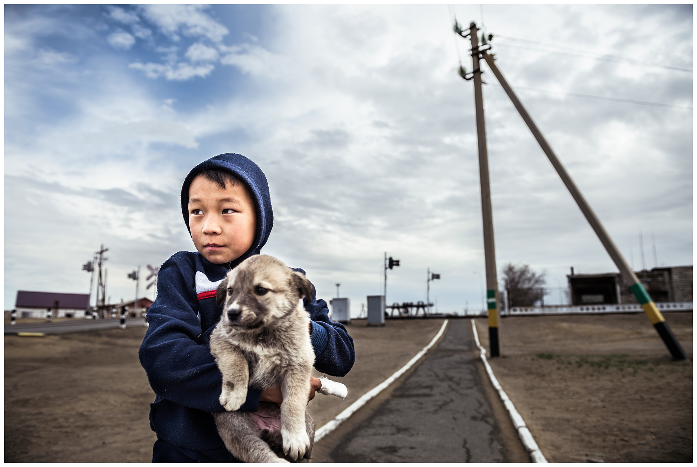 A boy standing with a puppy on a road from Aral
