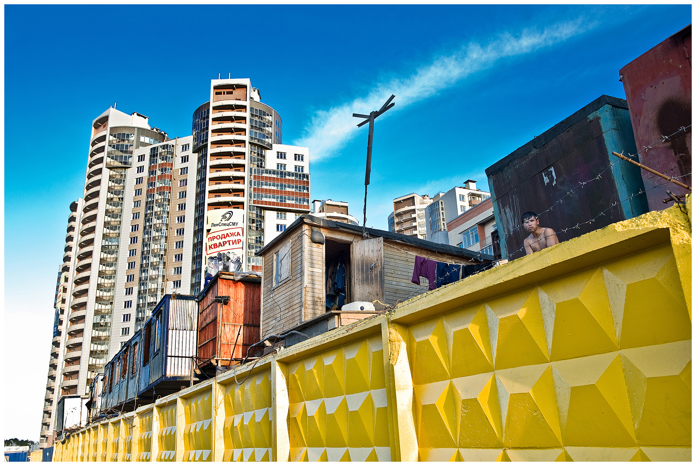 Saint Petersburg, Russia. An Asian guest worker sits behind a barbed wire in front of his provisional apartment.