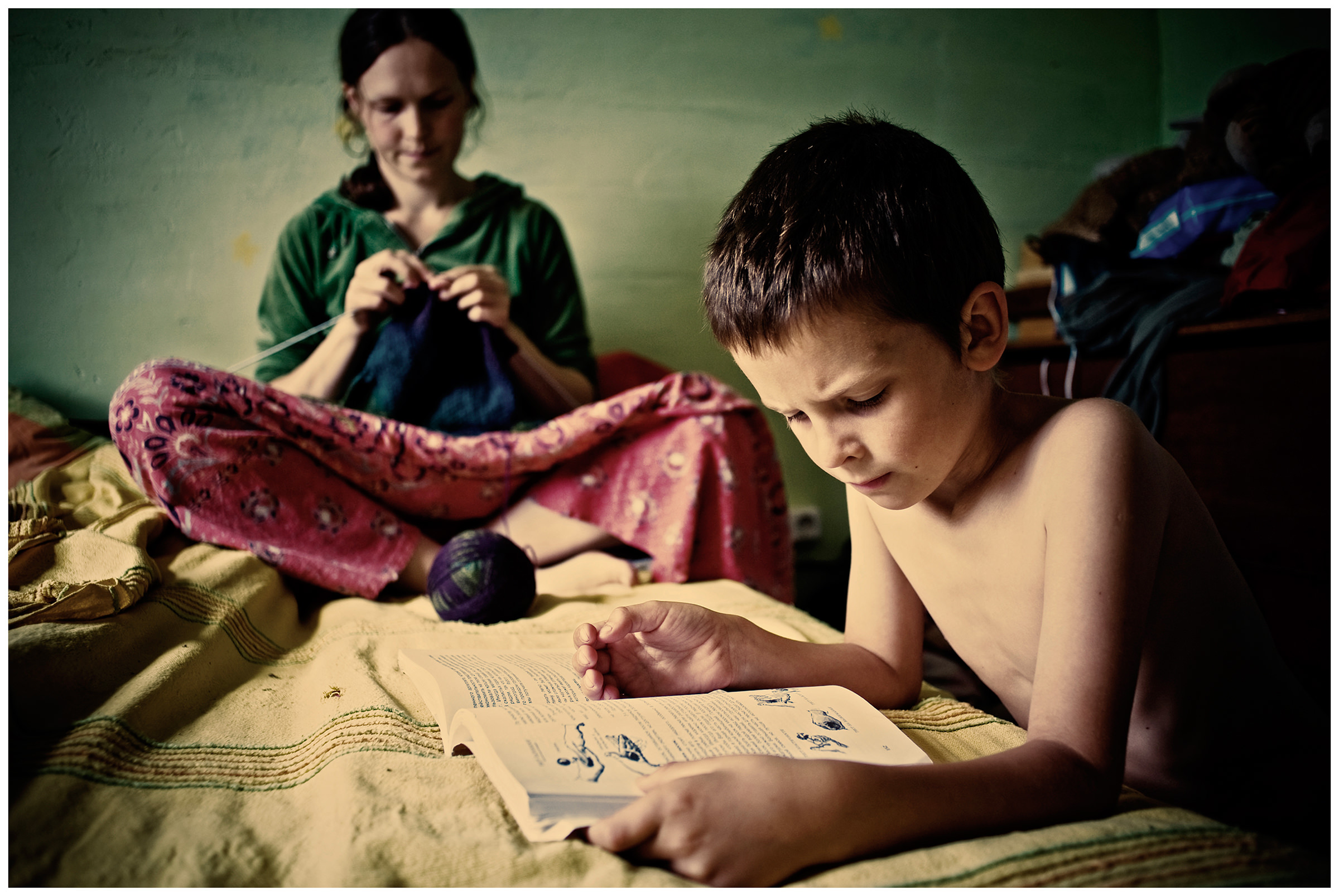 Belarus, village of Chereshlya. A boy reads a book and his mother knits.