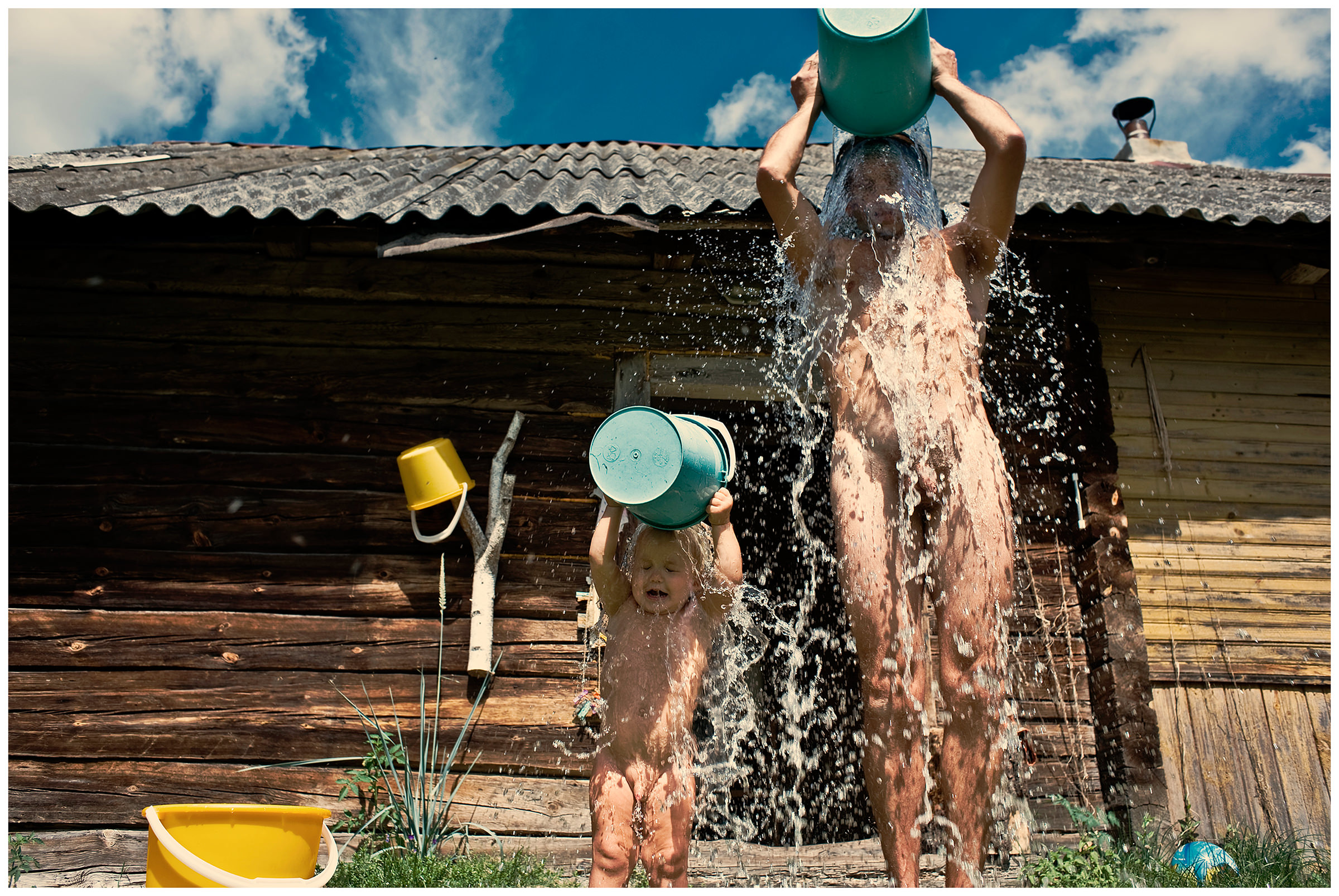 Belarus, village of Chereshlya. A man with his son water himself with water from the buckets.