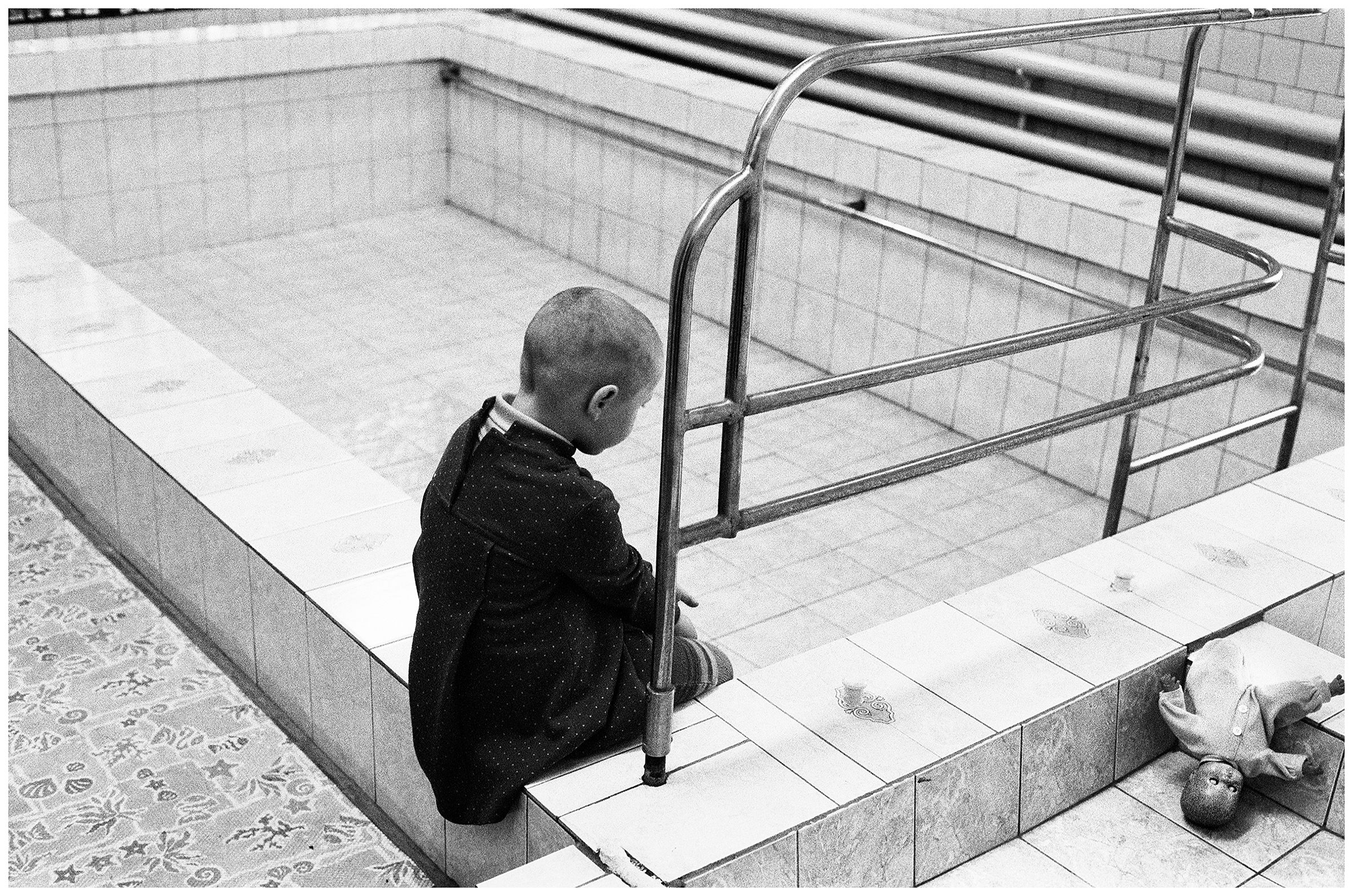 Minsk, Belarus. A girl with a doll sits at the edge of a swimming pool. The swimming pool has no water because the water in this district does not meet medical standards.