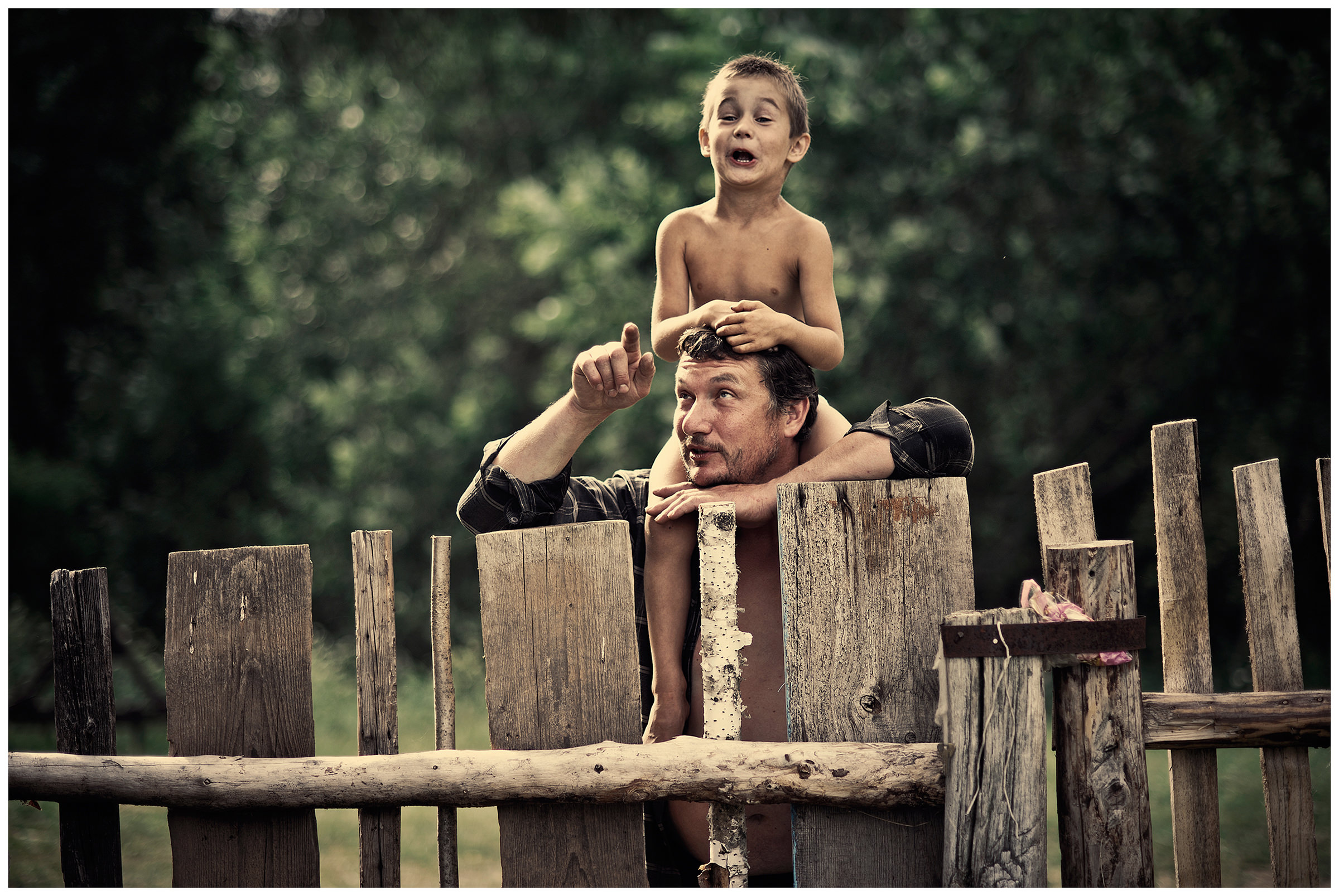 Belarus, village of Chereshlya. A boy stands with his father at a wooden fence.