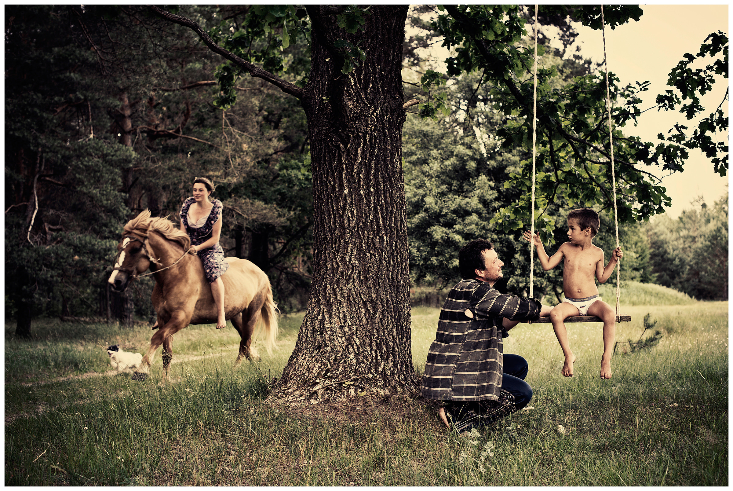 Belarus, village of Chereshlya. A man swings his child on a swing. A young woman is riding a horse.