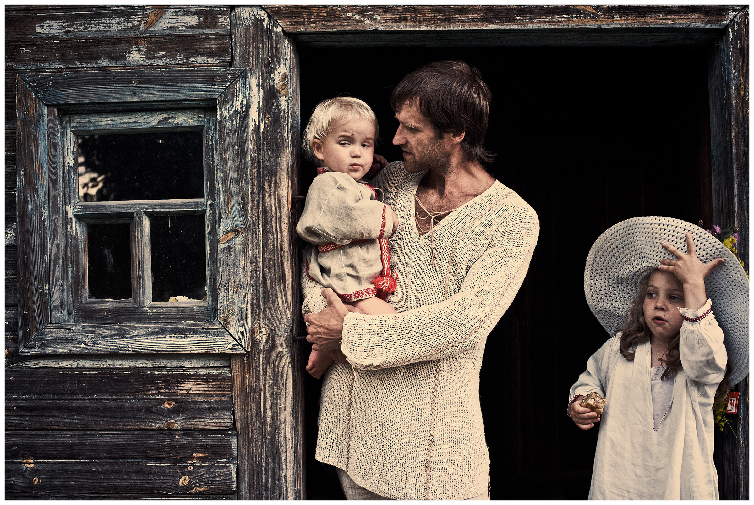 Belarus, village of Chereshlya. A man stands with his son and a girl at the threshold of a wooden house.