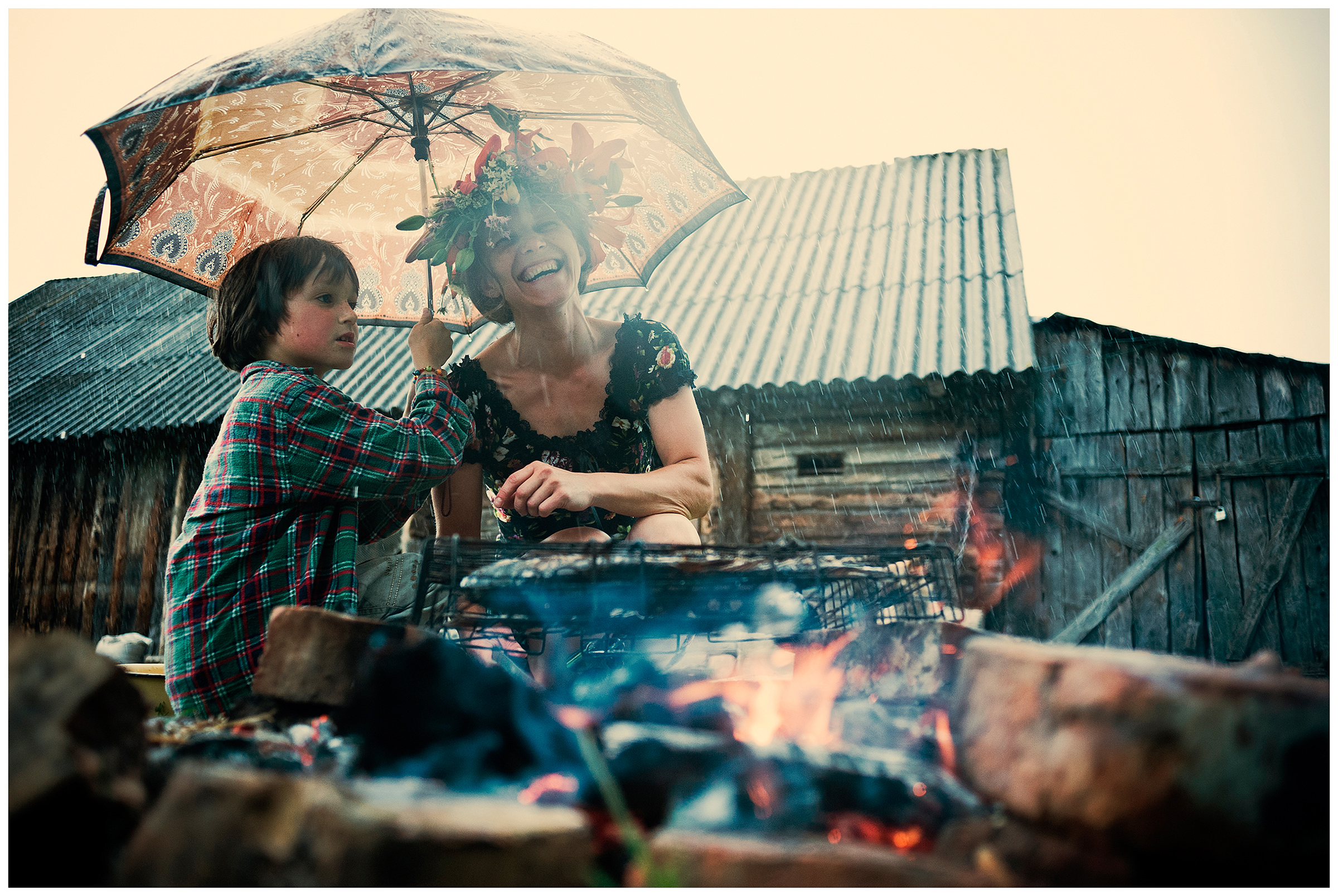 Belarus, village of Chereshlya. A woman and a boy roasting fish at a campfire under the rain.