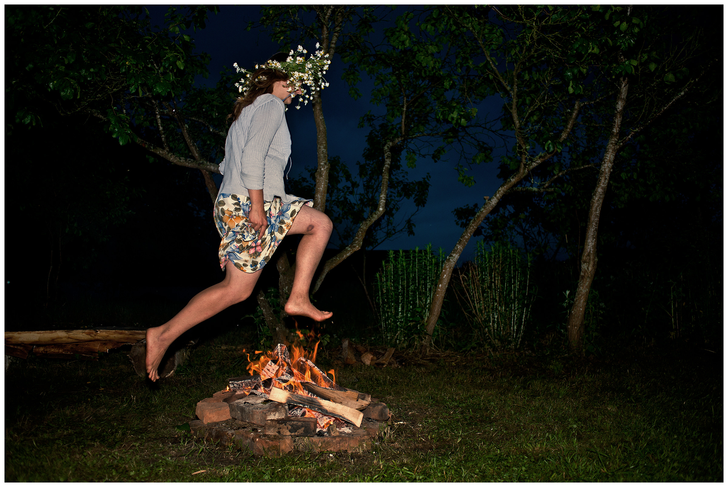 Belarus, village of Chereshlya. A young woman jumps over campfires at night.