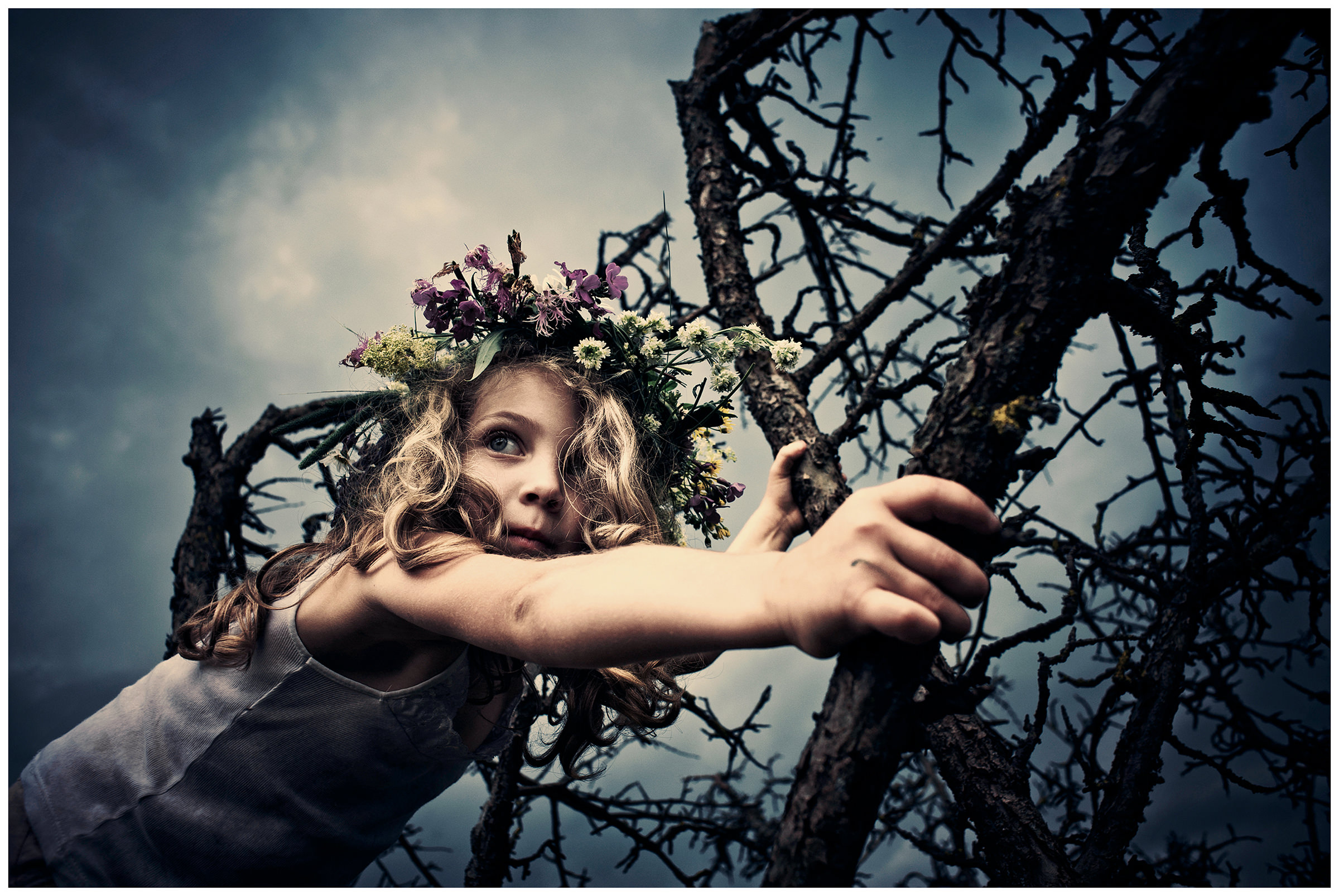 Belarus, village of Chereshlya. A girl crawling on a dry tree with a wreath of flowers on her head.