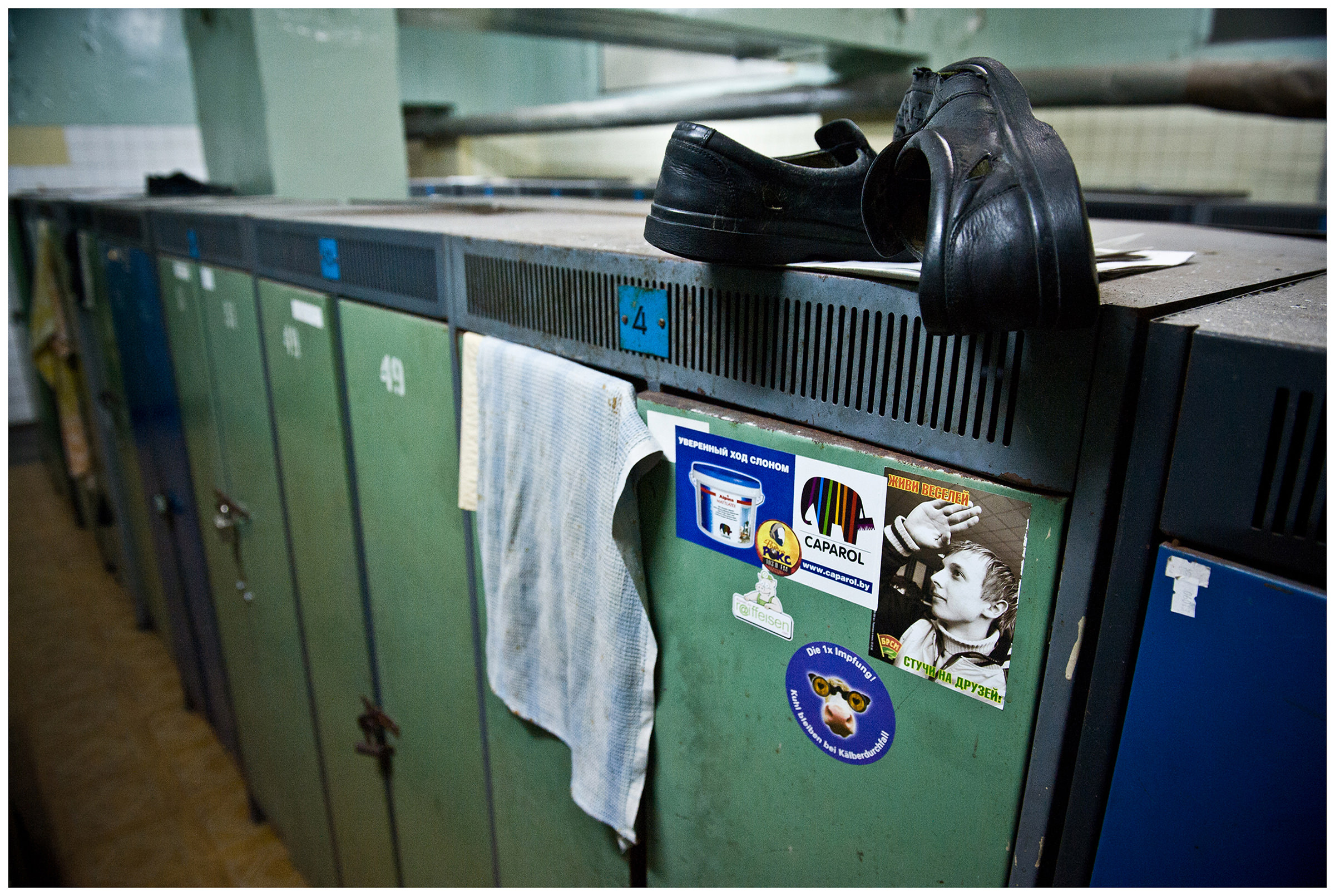 The work shoes lie on a locker in the changing room. The sticker on the locker is an anti-advertisement for the Belarusian Republican Youth Union with the slogan "Live happier, tell your friends off".