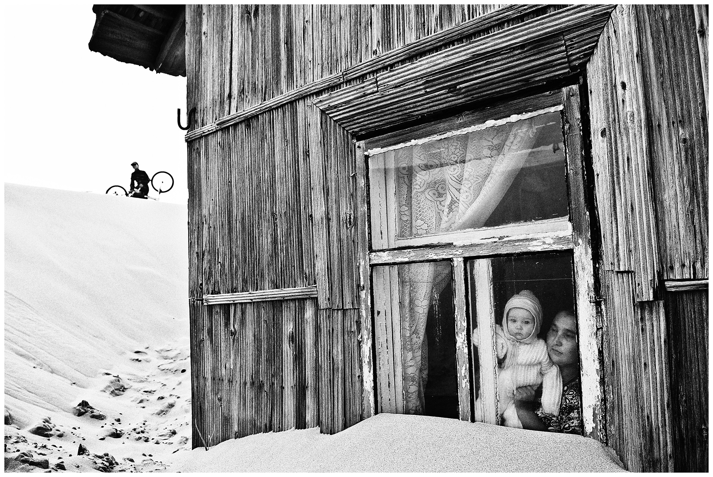 Shoyna village, Russia. A woman with a child looking out the window in a wooden house.