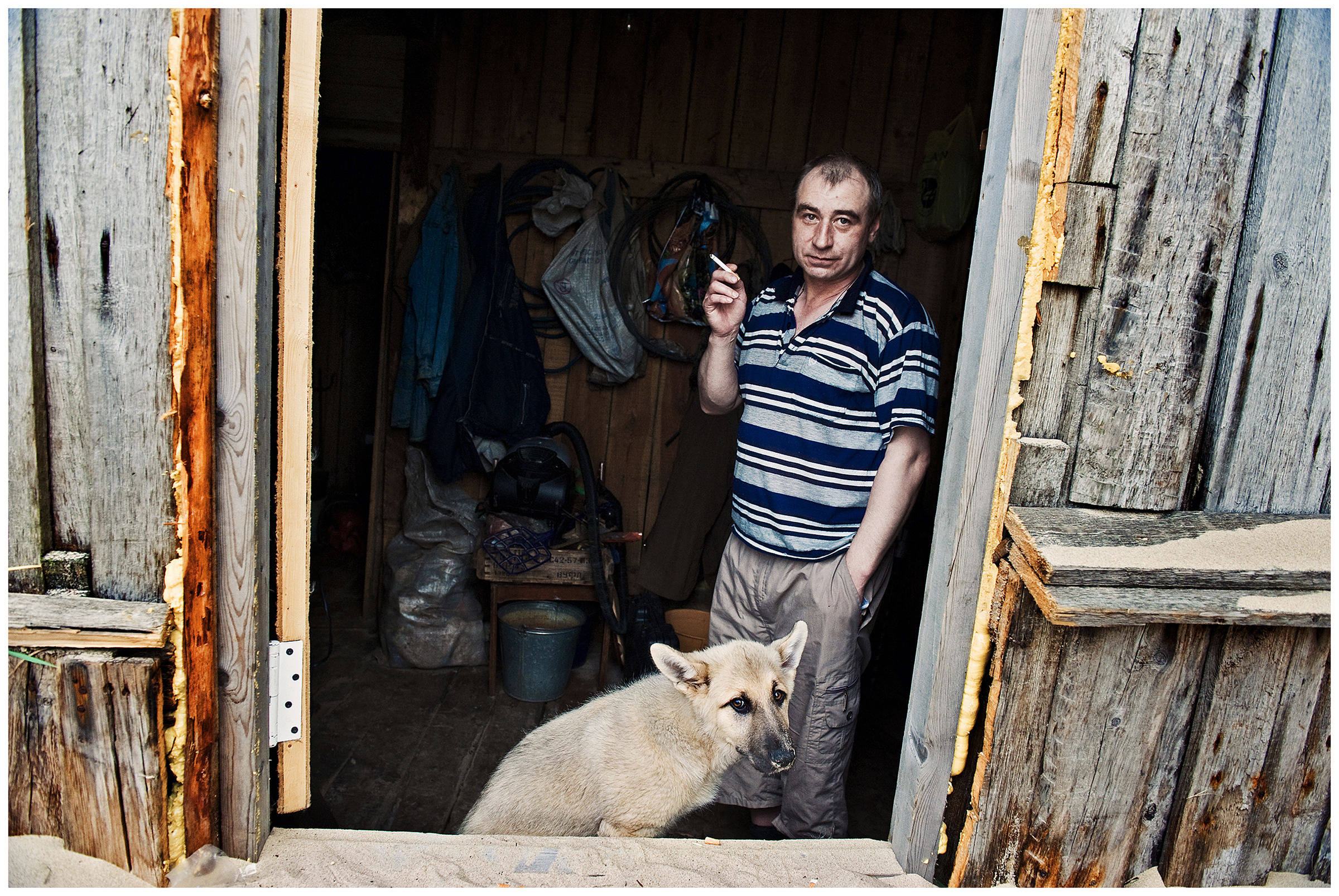 Shoyna village, Russia. A man with his dog stands on the threshold of his house.