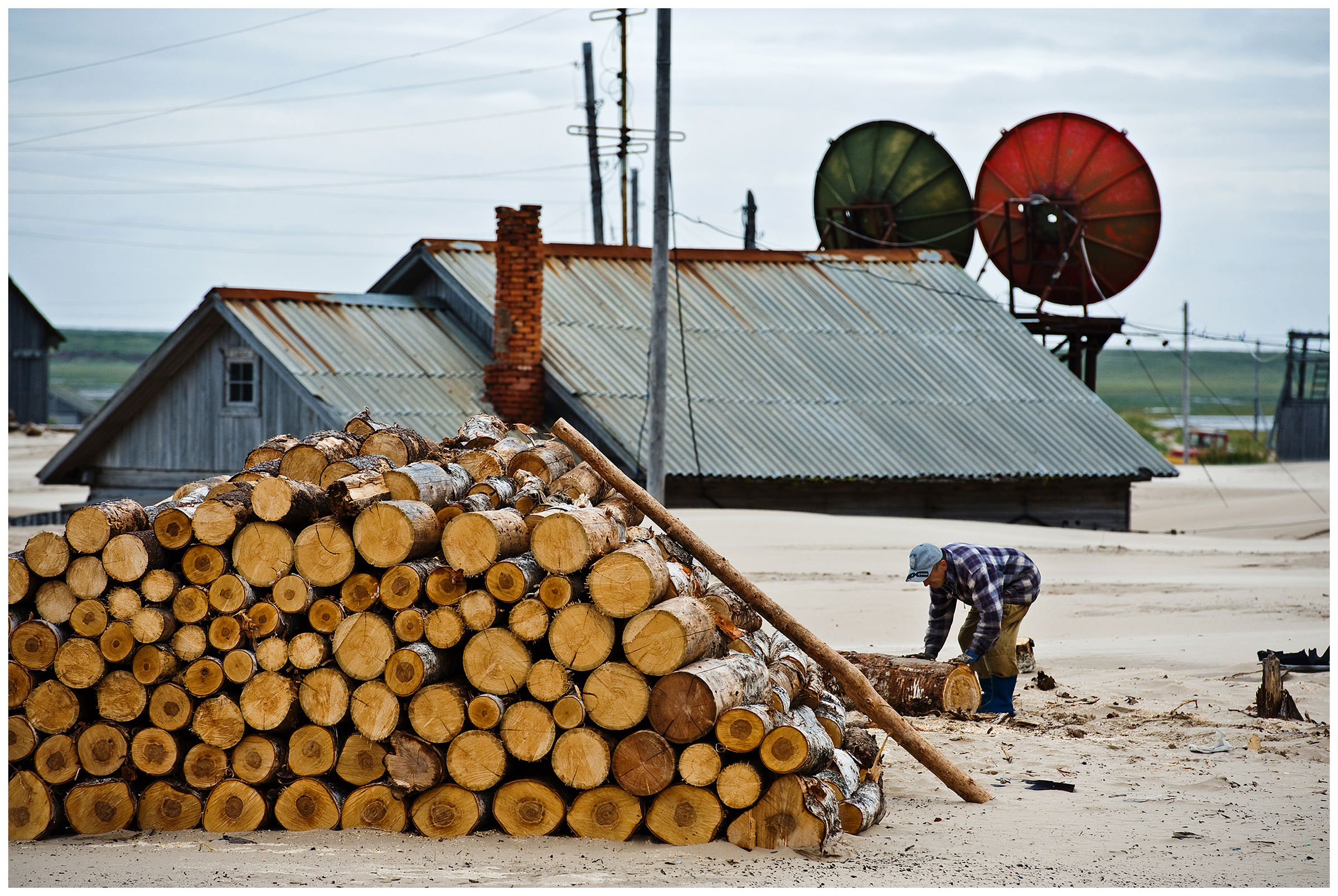 Shoyna village, Russia. A man chops wood in front of a house with a satellite dish.