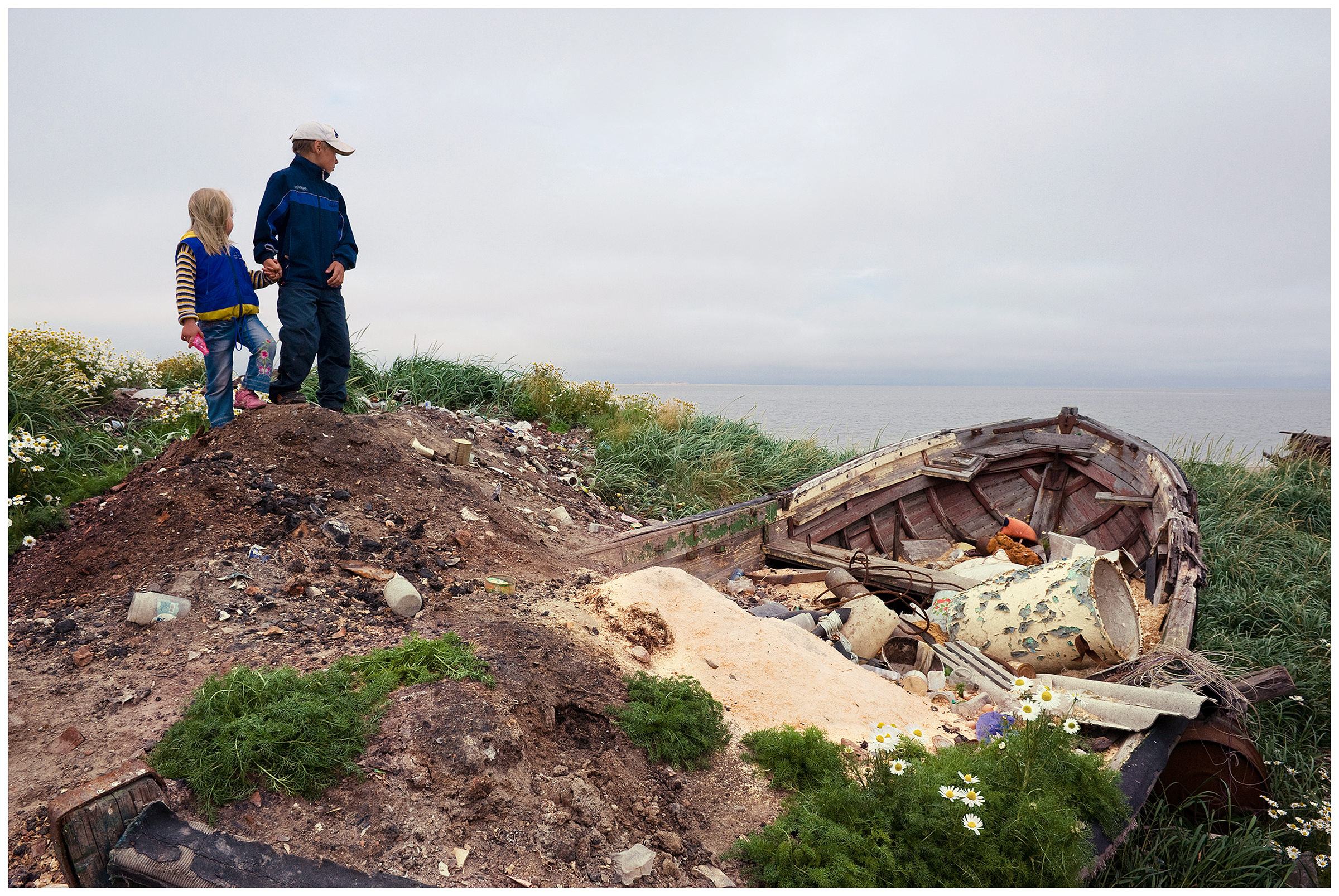 Shoyna village, Russia. A boy and a girl stand next to an abandoned boat on the seashore.