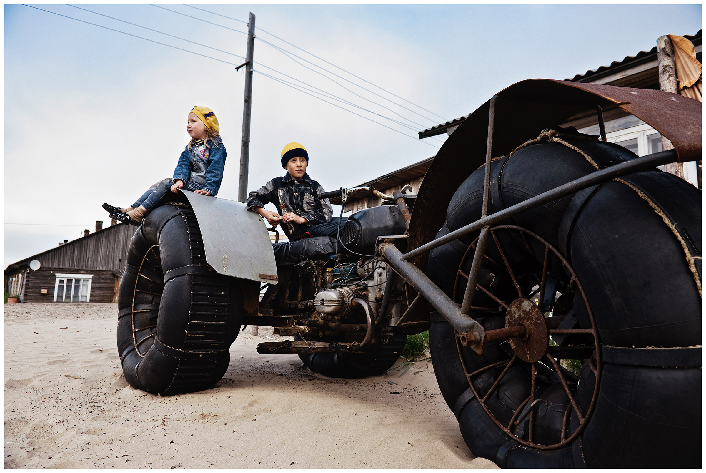 Shoyna village, Russia. A boy and a girl sit on a homemade vehicle of their father.