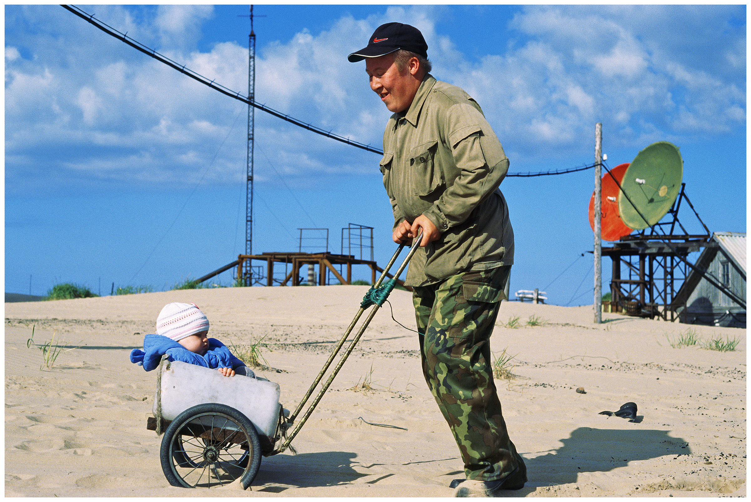 A man rolls a self-made baby carriage with a child through the sand