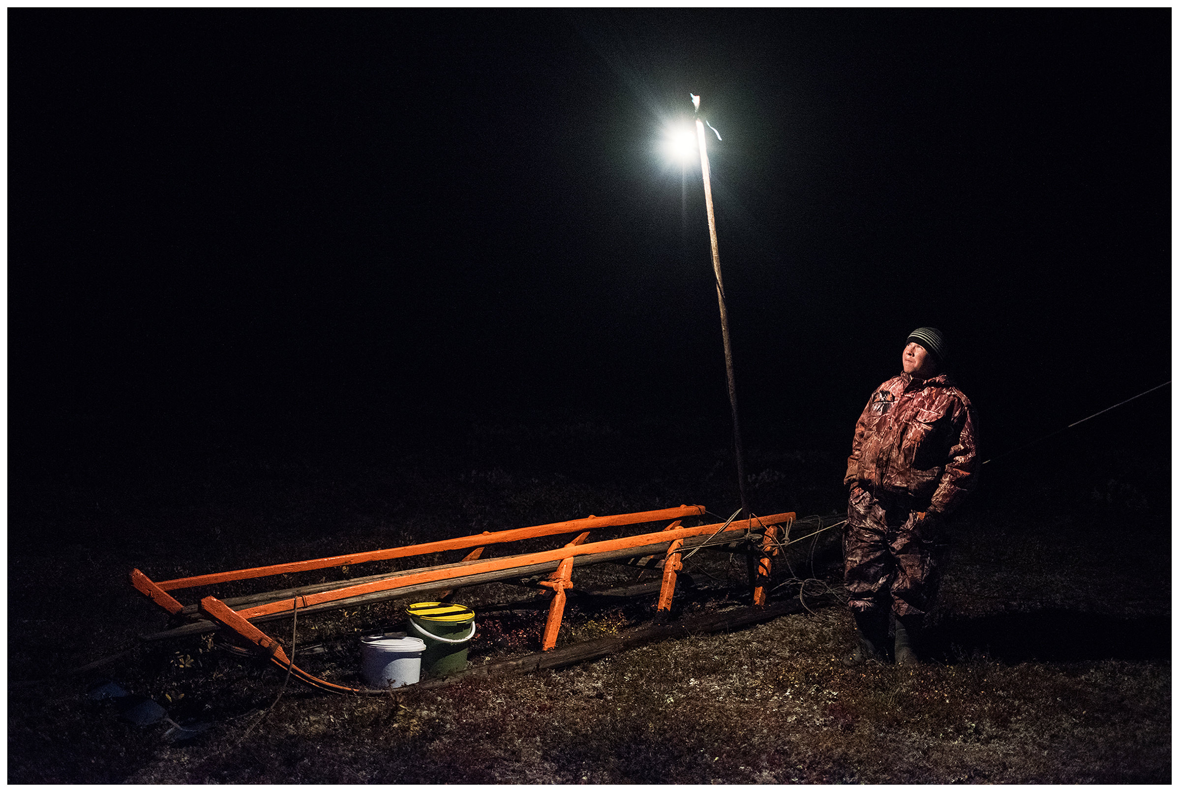 Nenets Autonomous Okrug, Komi Republic, Russia. A reindeer herder stands in front of a light bulb at night.