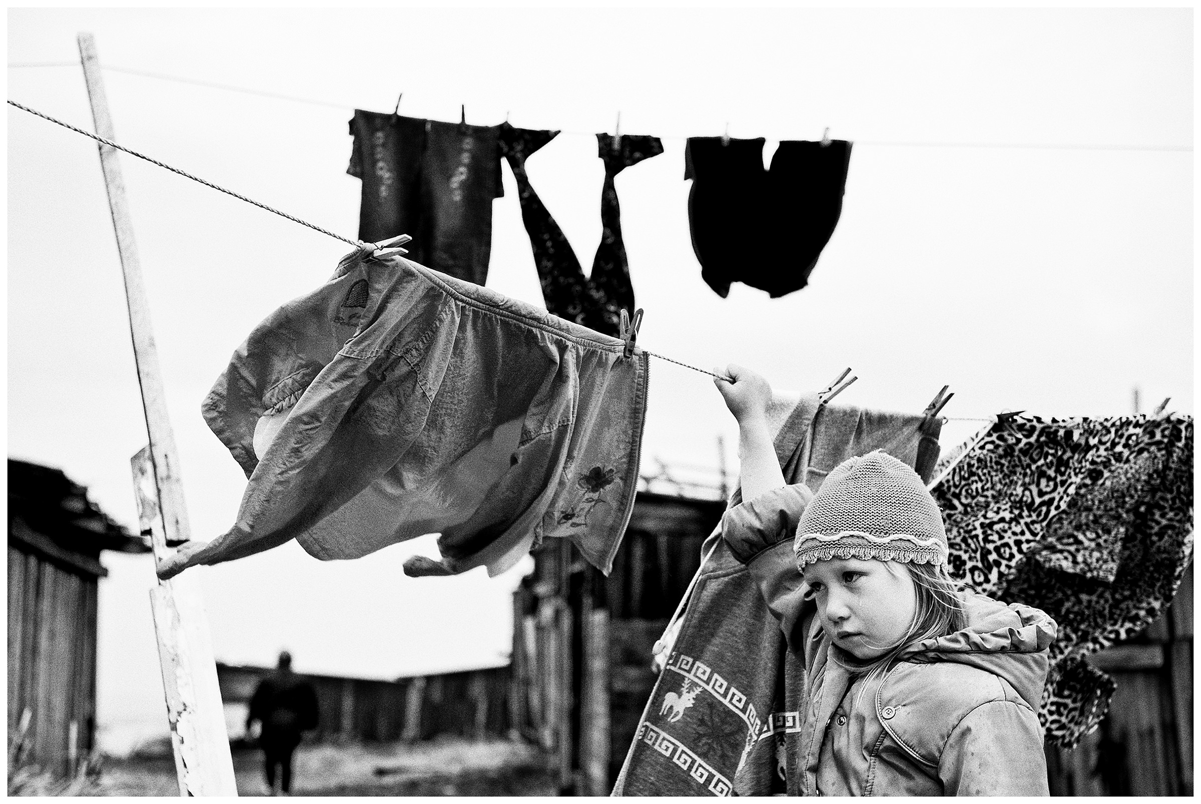 Shoyna village, Russia. A girl stands crying in front of a clothesline.