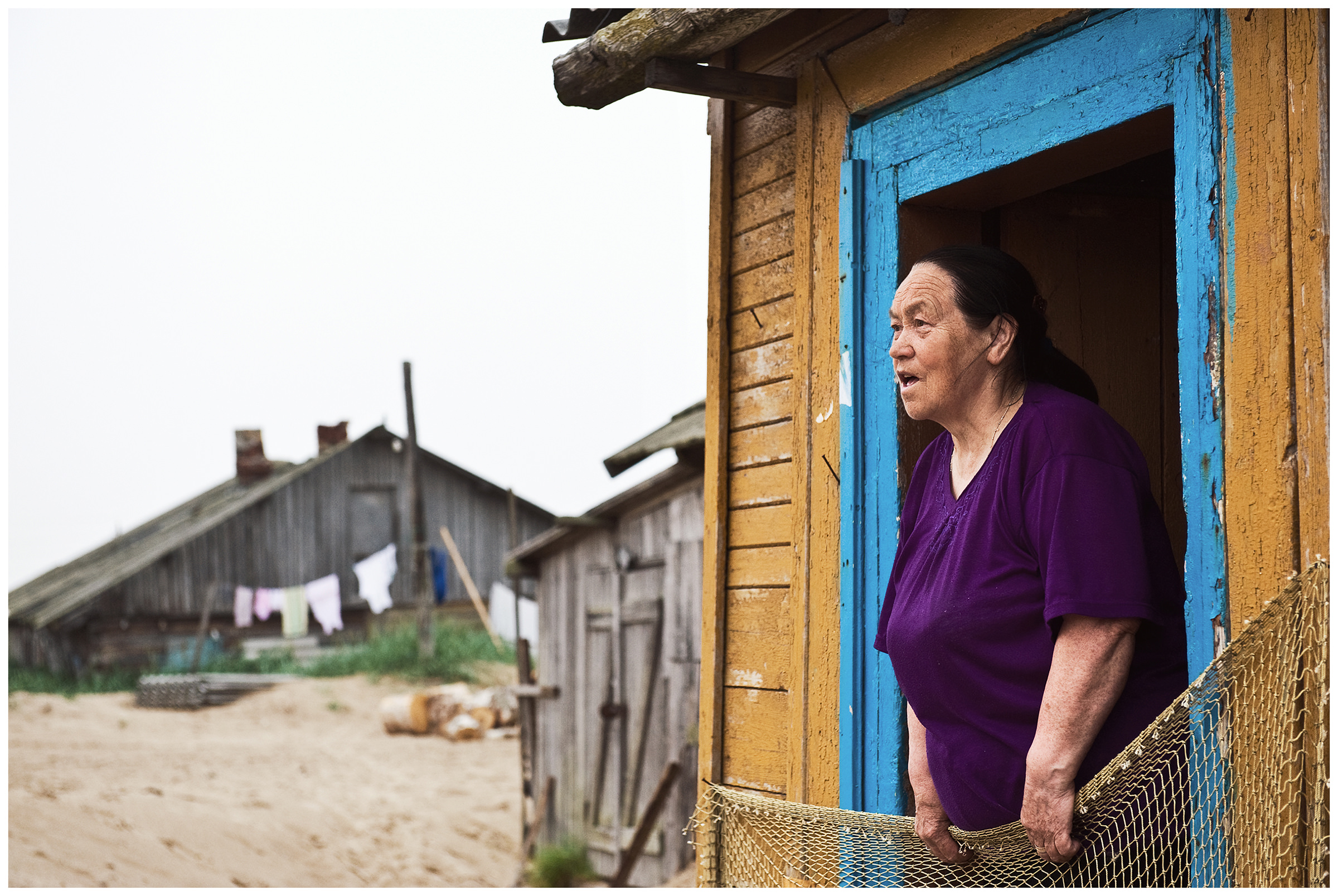 Shoyna village, Russia. A woman is standing on the threshold of her house.