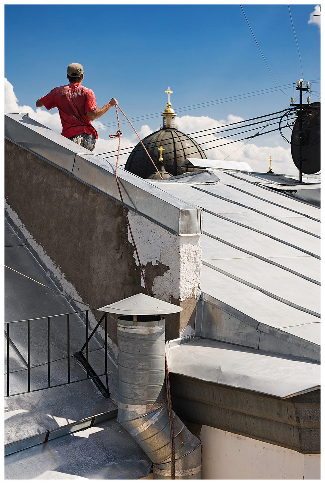 Saint Petersburg, Russia. A guest worker stands on a roof and pulls the ropes of an external elevator.