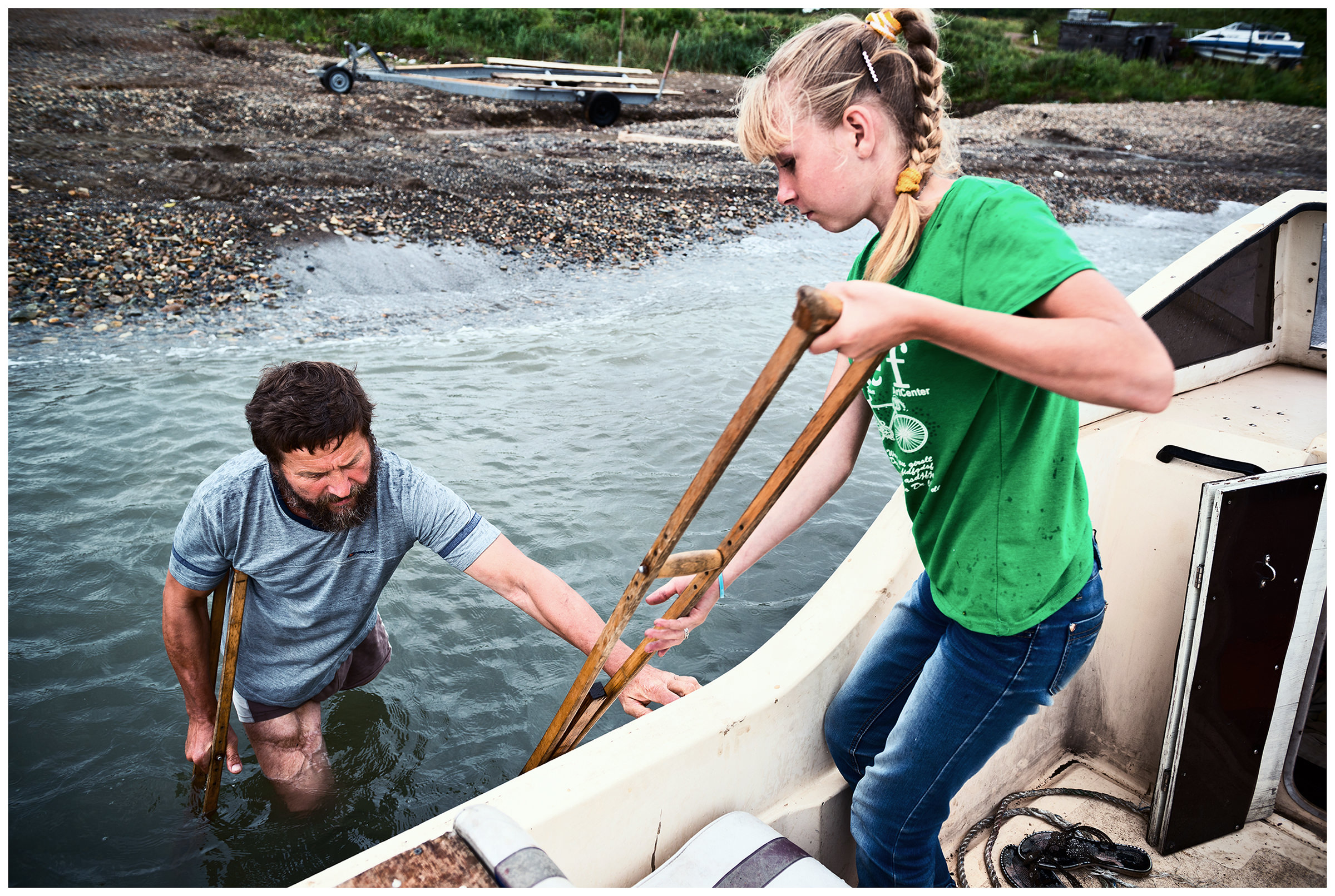 Ryazanovka village, Primorye, Russia. A man on crutches enters his cutter with the help of his daughter.