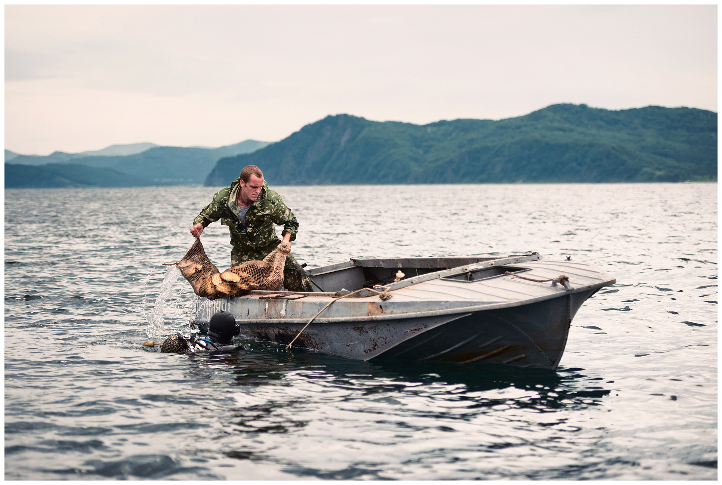 Peter the Great Bay, Sea of Japan, Russia. An illegal diver hands over the captured scallops to his colleague.