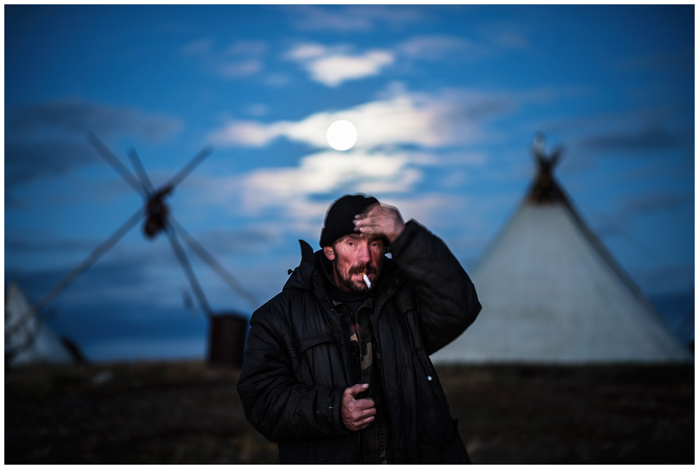 Nenets Autonomous Okrug, Komi Republic, Russia. A reindeer herder smokes in front of his tent.