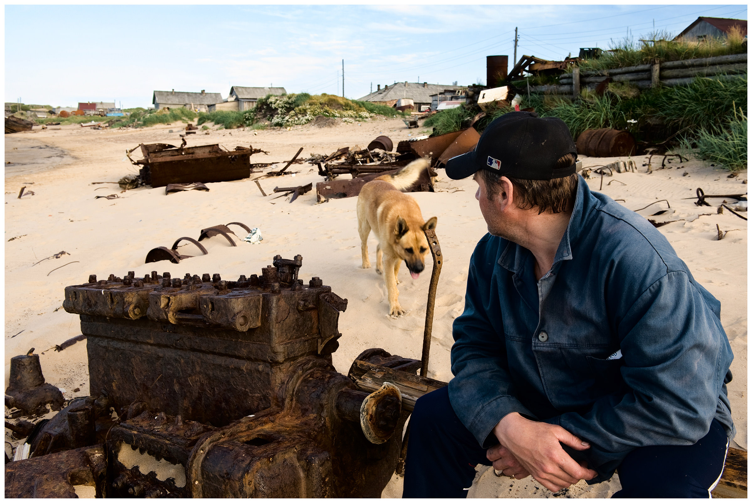 Shoyna village, Russia. A man with his dog sits on a ship wreck on the coast.
