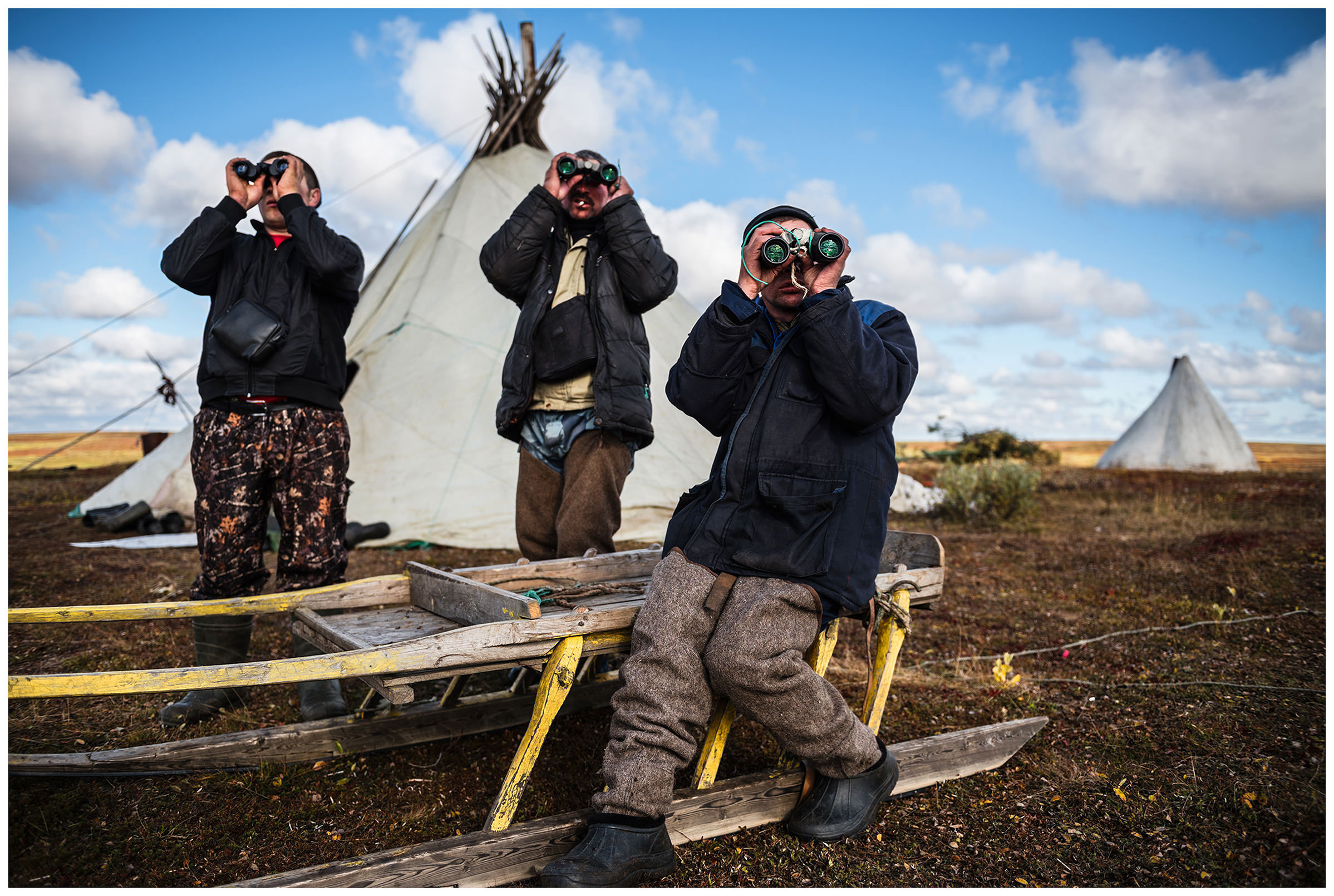 Nenets Autonomous Okrug, Komi Republic, Russia. Reindeer herders sit in front of their tents with binoculars.