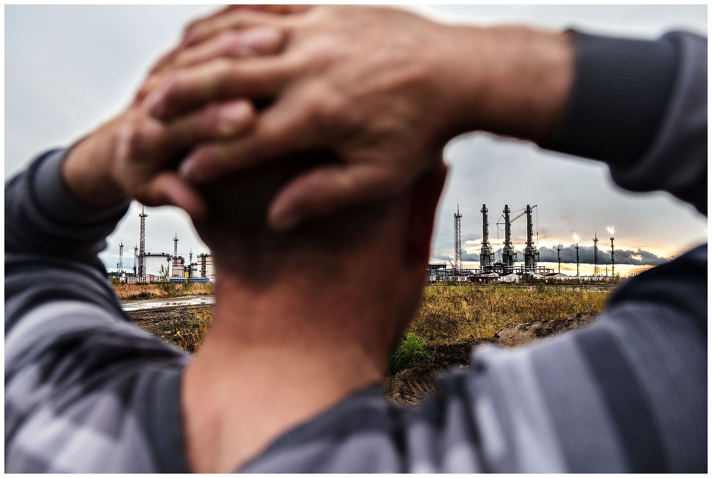 Nenets Autonomous Okrug, Komi Republic, Russia. A reindeer herder stands in front of an oil field.
