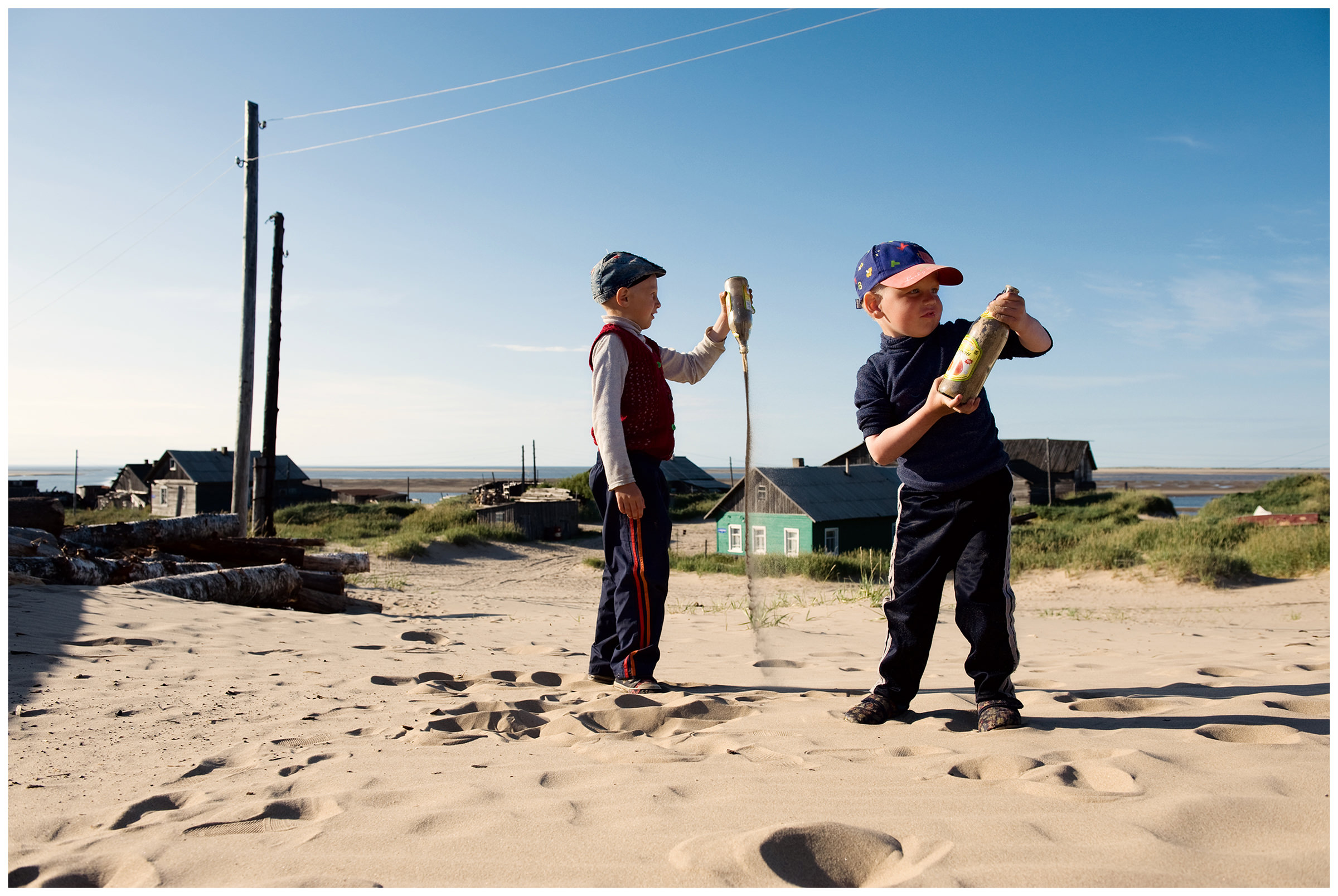 Shoyna village, Russia. Two boys play with two bottles in the sand.