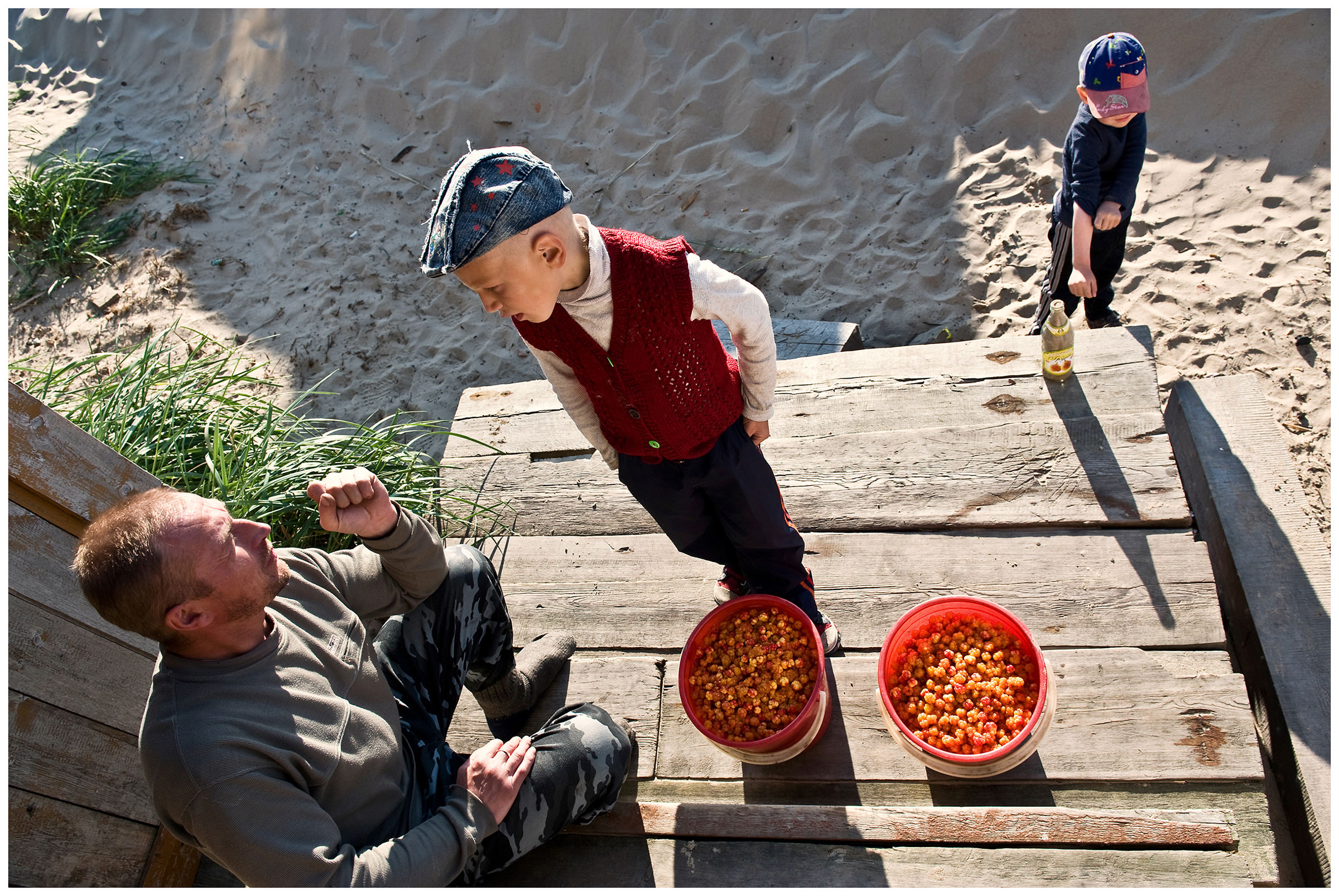 Shoyna village, Russia. A boy and his father talk next to two buckets of cloudberries.