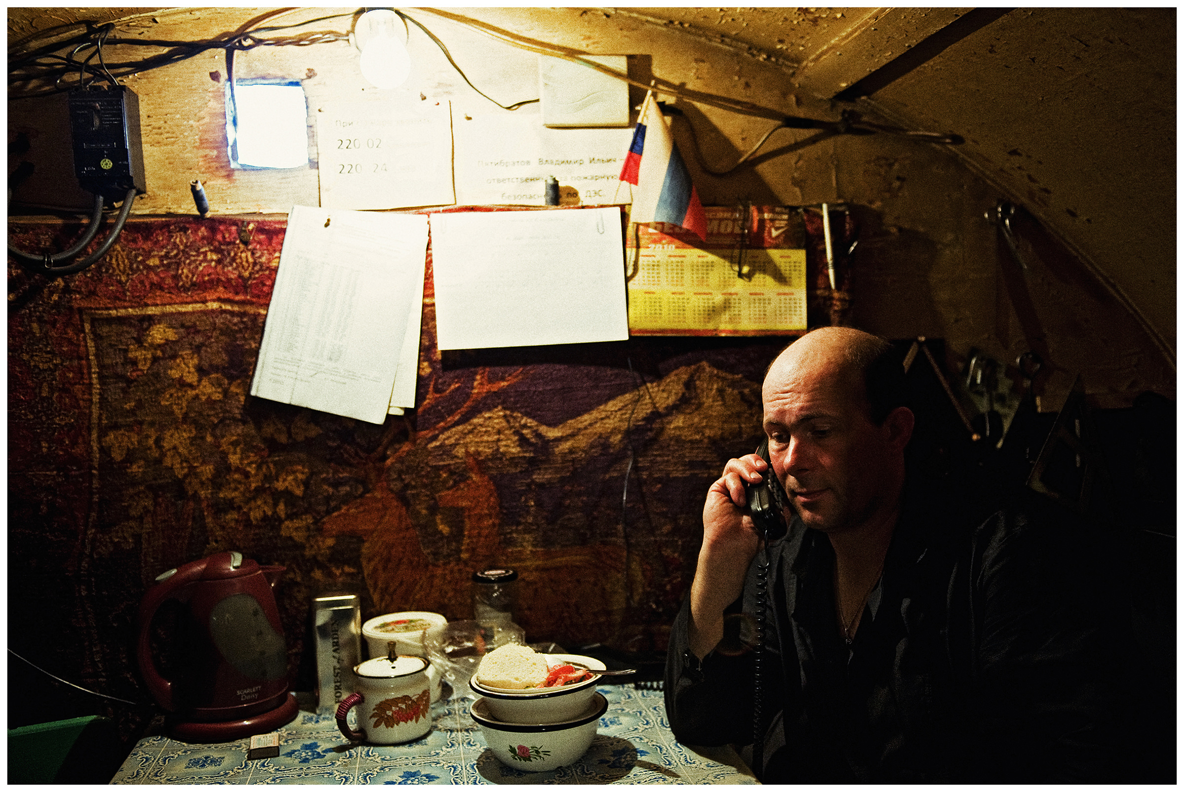 Shoyna village, Russia. A man eats and phones at his workplace at a diesel station.