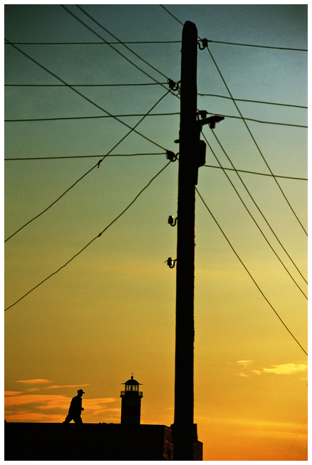 Shoyna village, Russia. A man walks on a roof of a house in front of the lighthouse at sunset.