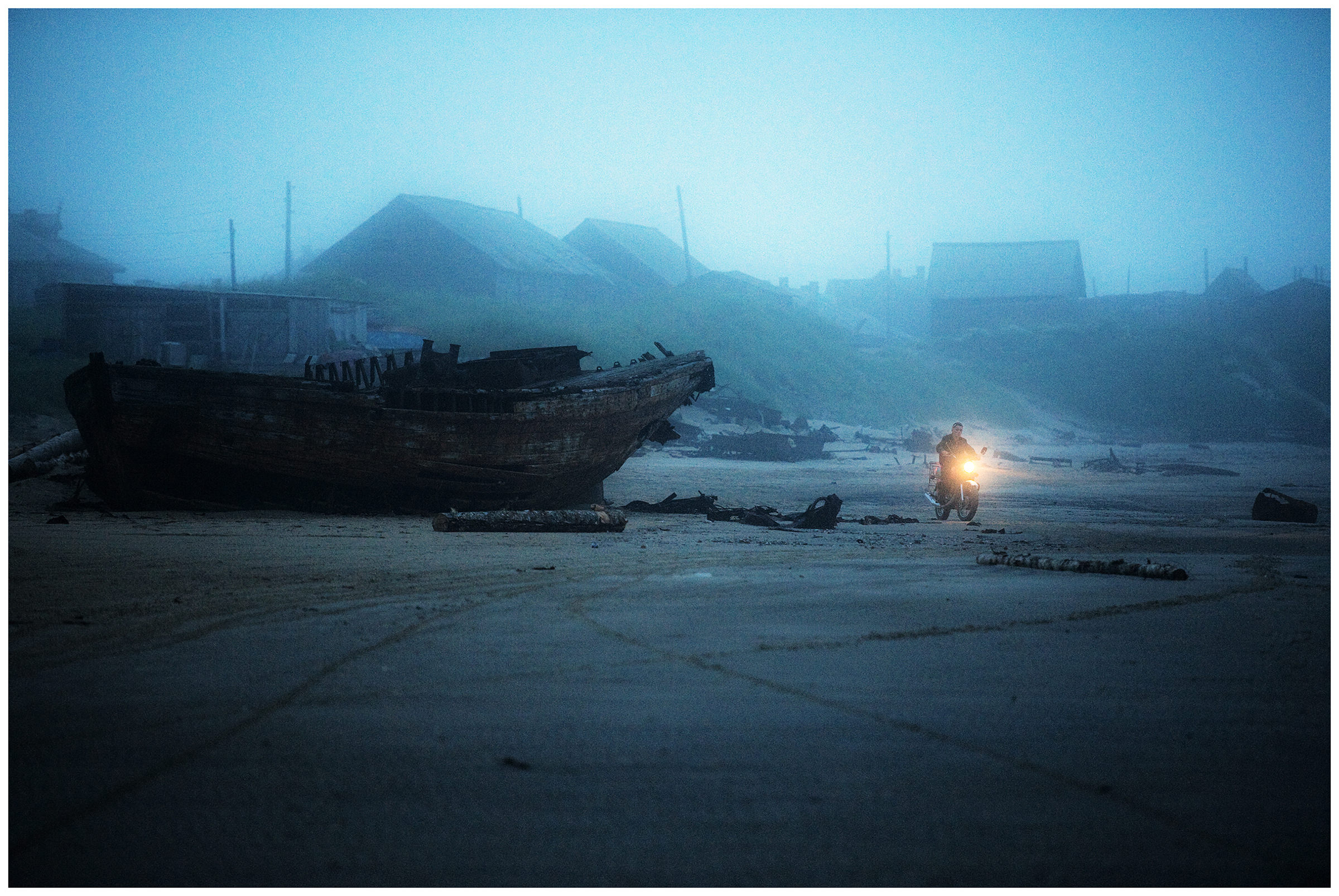 Shoyna village, Russia. A motorbike drives along the coast past the shipwrecks.