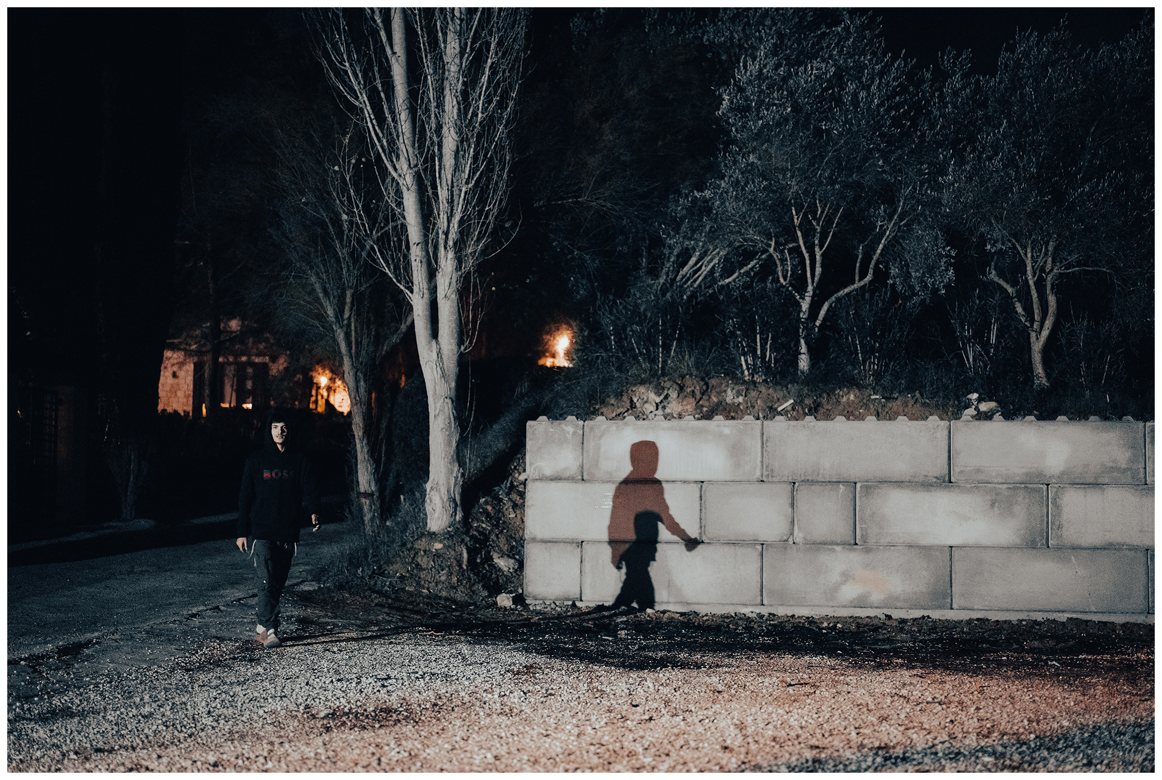 Miliou, Cyprus. An Israeli walks to a campfire in the Secret Forest wellness retreat late in the evening and casts a shadow on a wall.
